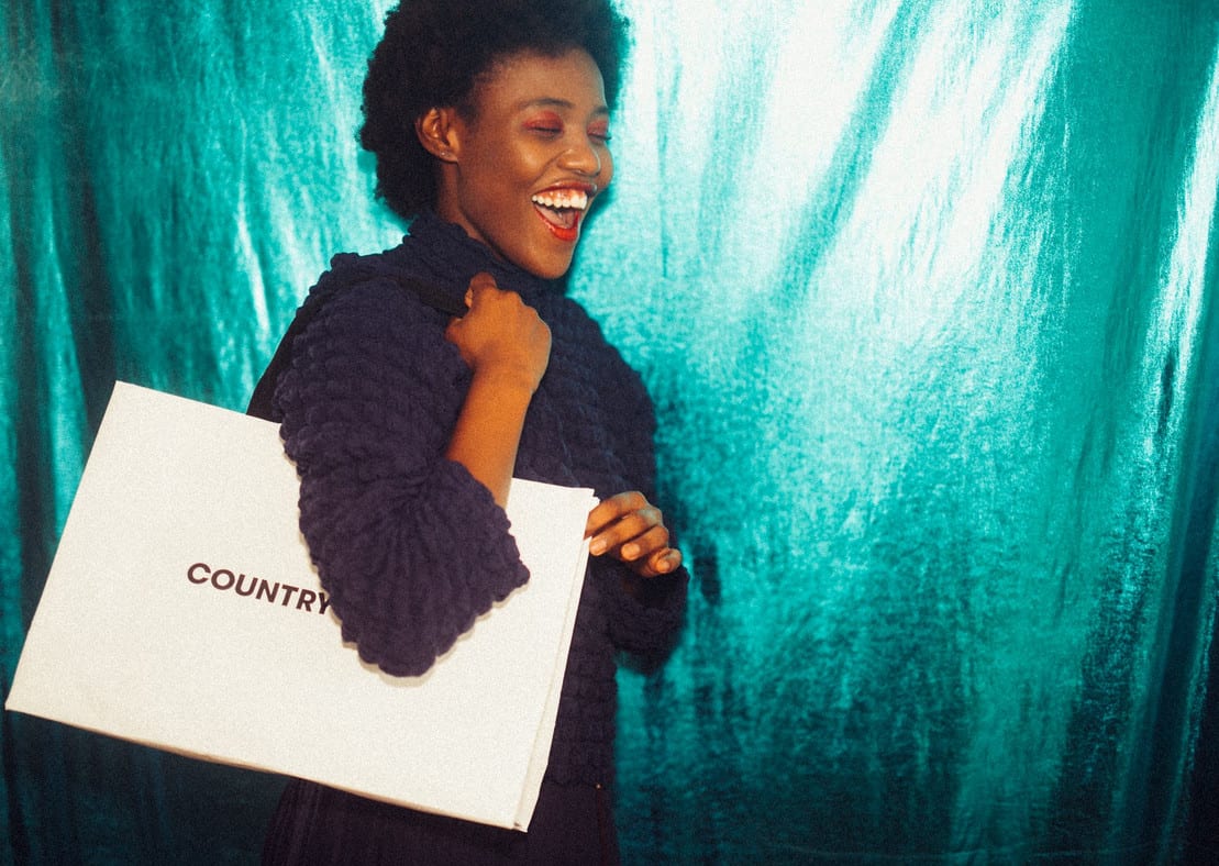 Mulher negra com sorrisão e sacola de compras