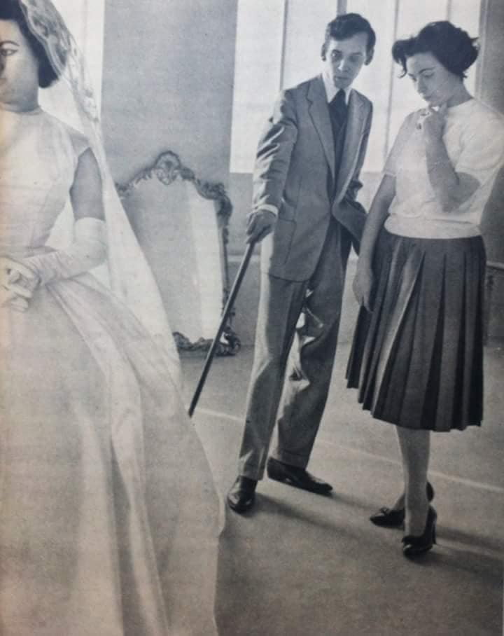 Dener Pamplona jovem a avaliar uma modelo com um vestido de noiva branco.