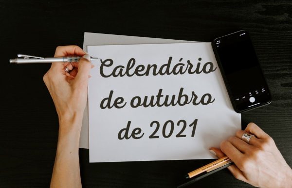 Foto de mãos de mulher escrevendo “Calendário de outubro de 2021” em uma folha branca usando lapiseira