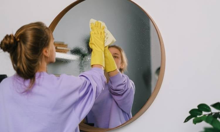 Mulher limpando espelho com pasta de dente.