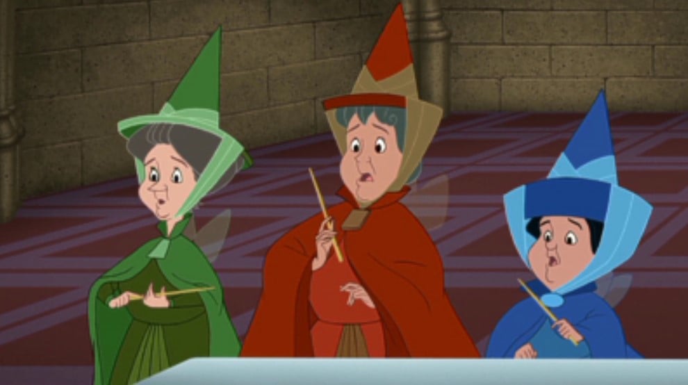 Imagem das três fadas do filme "A Bela Adormecida", Fauna, Flora e Primavera, vestidas com roupas inspiradas no traje gótico em azul, verde e vermelho, com chapéu pontiagudo e véu