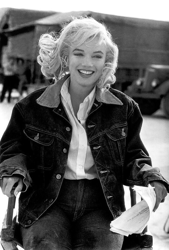Foto em preto e branco de Marilyn Monroe sentado e sorrindo vestida com jaqueta e calça jeans Foto em preto e branco de Marilyn Monroe sentado e sorrindo vestida com jaqueta e calça jeans