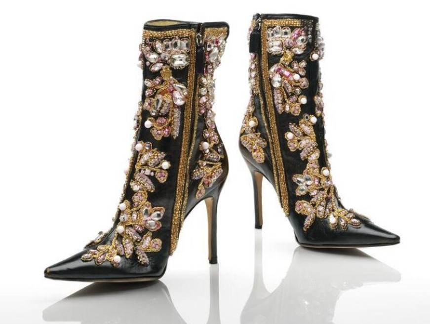 Foto de um par de botas pretas de couro de salto alto fino com zíper e adornadas com pedrarias e bordados dourados em um fundo branco Foto de um par de botas pretas de couro de salto alto fino com zíper e adornadas com pedrarias e bordados dourados em um fundo branco