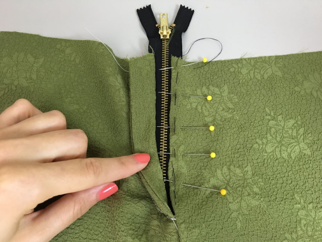 Foto de uma mão de mulher a mostrar o detalhe de uma roupa a ser costurada com um zíper