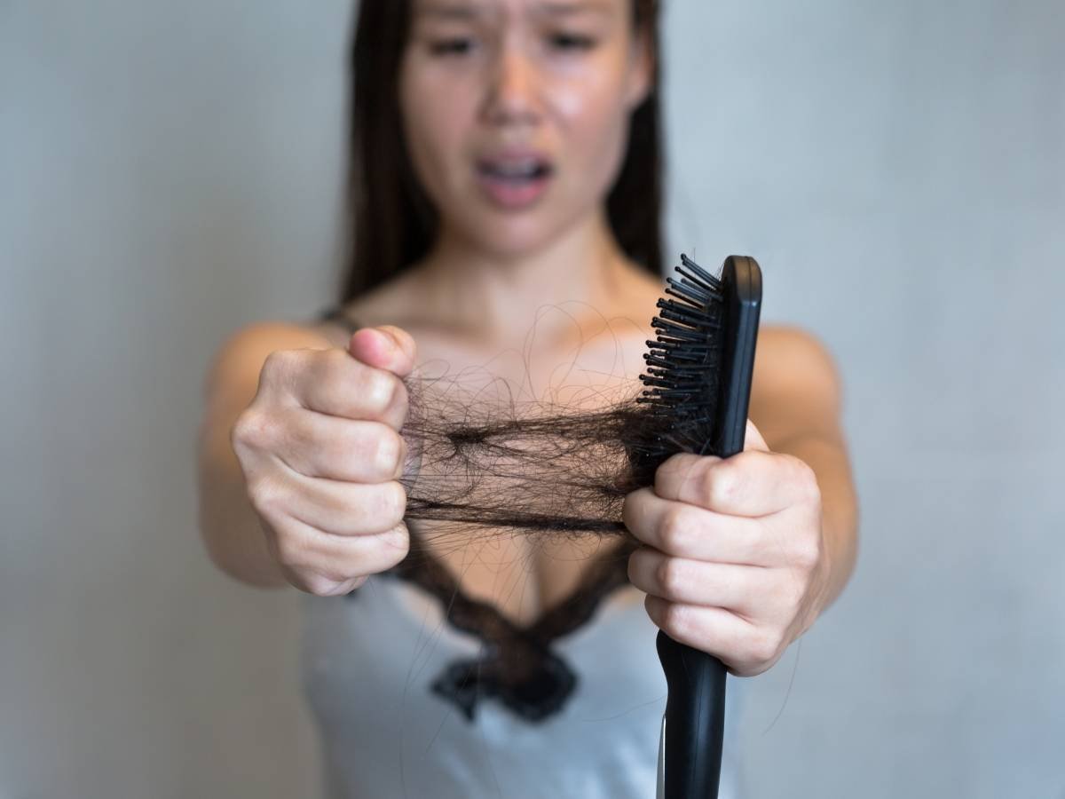 Mulher chocada com queda de cabelo na escova.
