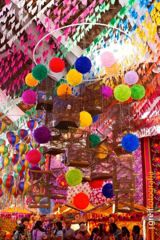 A imagem representa decorações de festa junina com cores neon, pompons de papel crepom coloridos