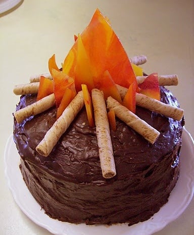 A imagem representa decorações de festa junina: bolo de chocolate com fogueira falsa no topo
