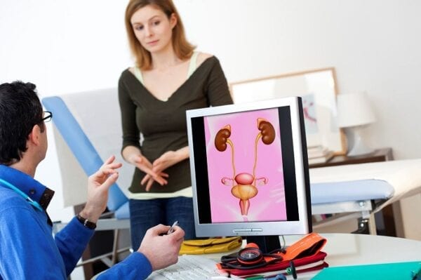 Infecção urinária - Foto de mulher em consultório médico e este com imagem do aparelho urinário na tela do computador