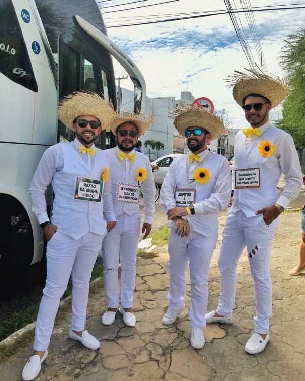 Homens de branco com flor de girassol, chapéu de palha e plaquinhas sobre festa junina