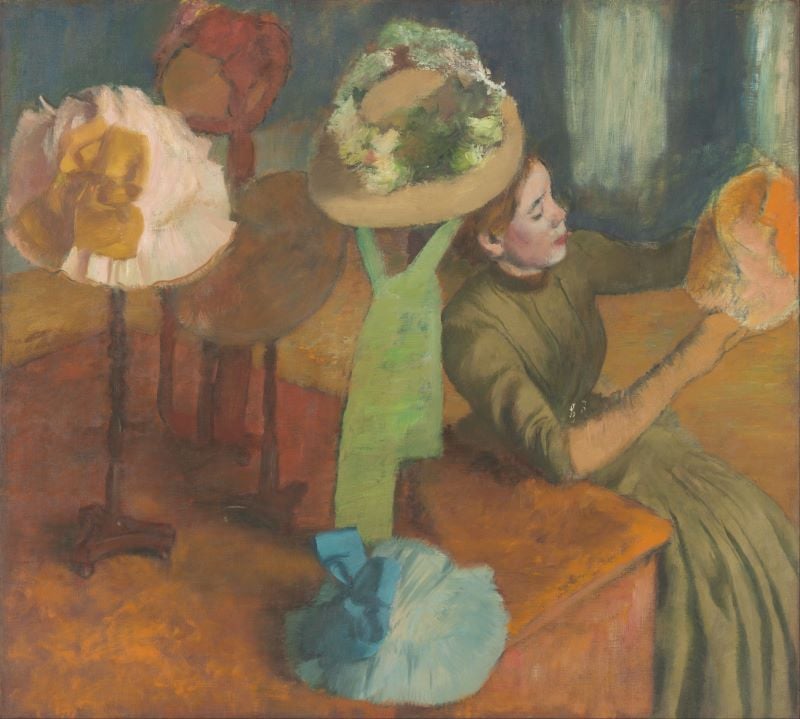 Mulher em uma chapelaria sentada com um chapéu na mão