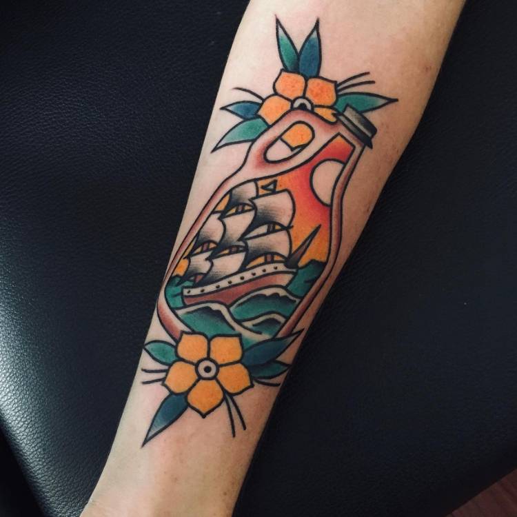 Pessoa de pele clara com braço tatuado de garrafa com barco e flores ao redor estilo old school