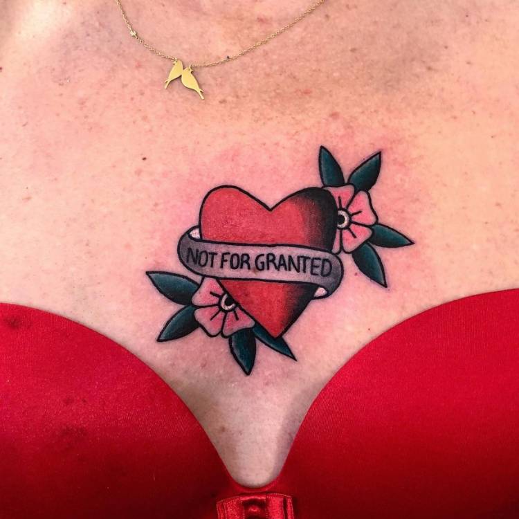 Mulher de sutiã vermelho com coração tatuado no peitoral, estilo old school com flores e escrito "not for granted"