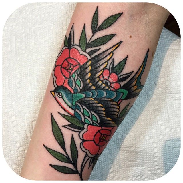 Pessoa de pele clara com tatuagem de andorinha e flores old school coloridas