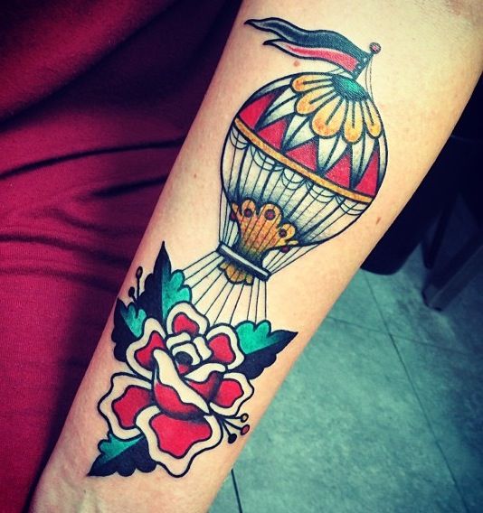 Pessoa de pele clara tatuada com balão old school colorido carregando uma grande flor vermelha