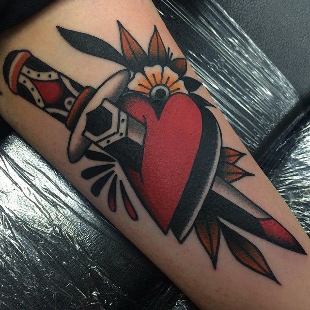 Tatuagem old school de adaga preta e vermelha enfiada em coração vermelho com flor amarela ao lado 