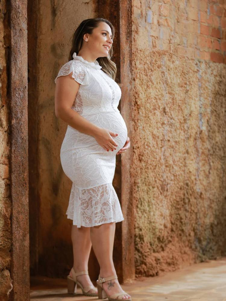 Mulher de pele clara grávida usando vestido de noiva curto com rendas
