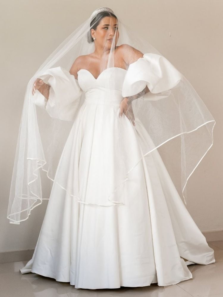 Mulher de pele clara usando vestido de noiva sem alça, mengas bufantes removíveis e véu 