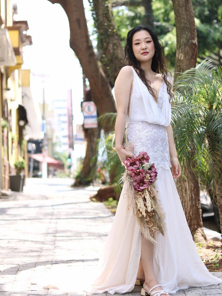 Mulher asiática na calçada usando vestido de noiva branco com babado no colo, saia curta, longa e buquê de flores rosas