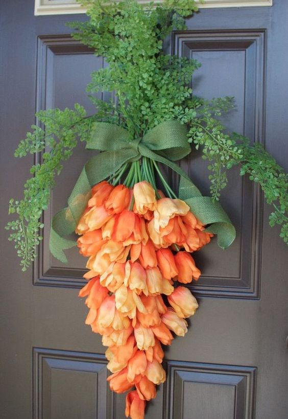 Cenoura feita de flores artificais laranja com ramos e laço verde