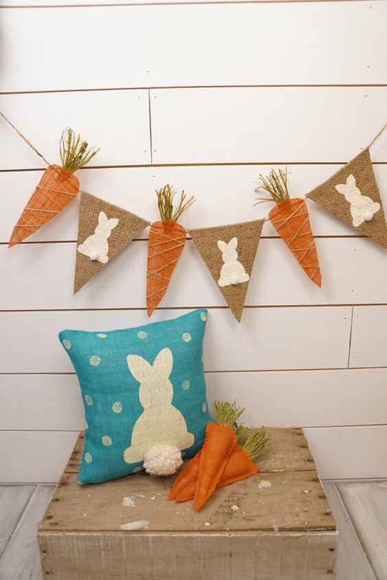 Varal de bandeiras de cenoura e coelhos em cima de almofada de coelho com enfeites de cenoura em feltro.