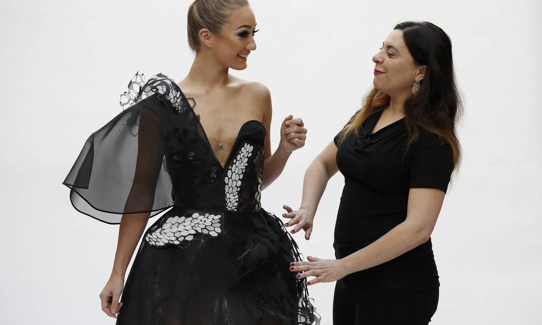 grafeno na moda Duas mulheres, uma vestindo um vestido preto e branco com detalhes em escama e a outra, de blusa preta, sorrindo e interagindo. A modelo olha para a mulher ao seu lado.