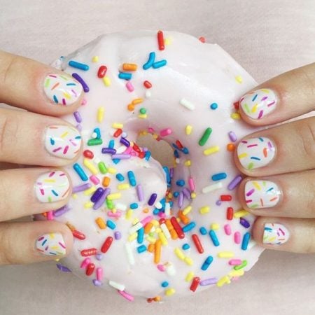 Unha branca de donuts, com mão segurando o doce