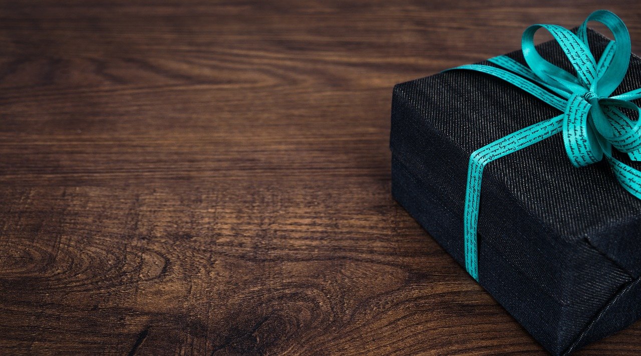 Foto de uma caixa de presente enrolada com fita azul em uma mesa de madeira