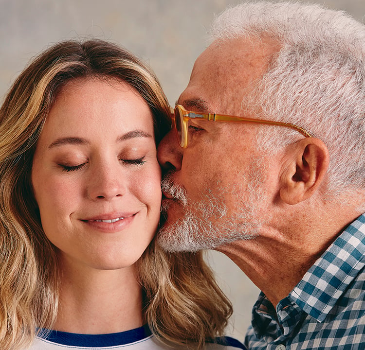 Um pai mais velho dá um beijo na bochecha da filha loira.