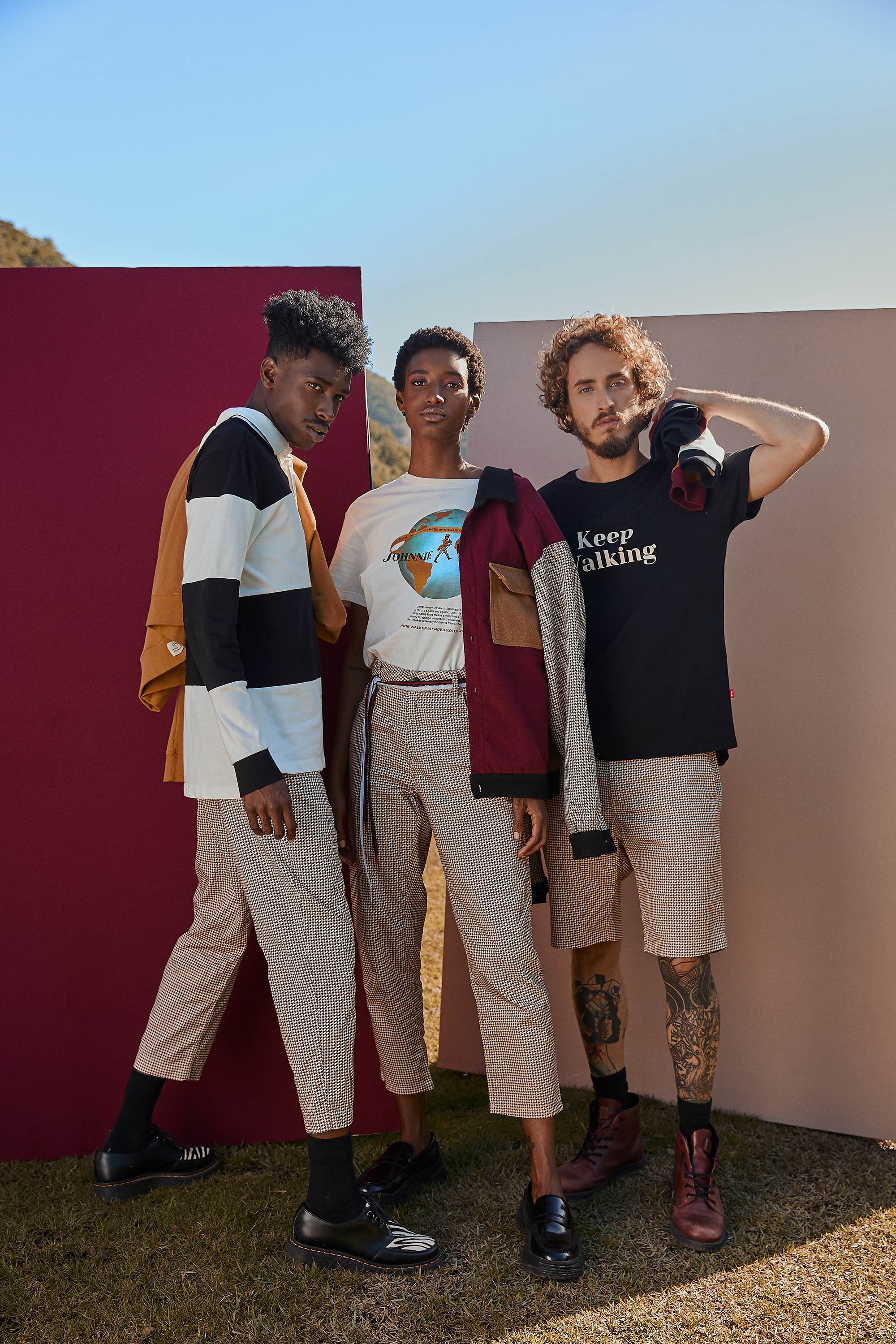 Três modelos em pé juntos, usando roupas de cores mostarda, vinho, branco e azul marinho
