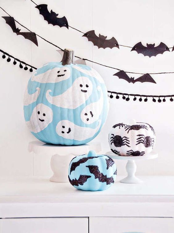 Foto de abóboras decoradas com desenhos de fantasmas, morcegos e aranhas para o Halloween.