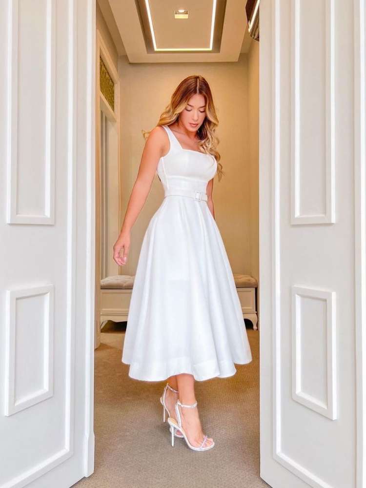 Mulher de pele clara e cabelo loiro usando vestido midi branco de alças e salto