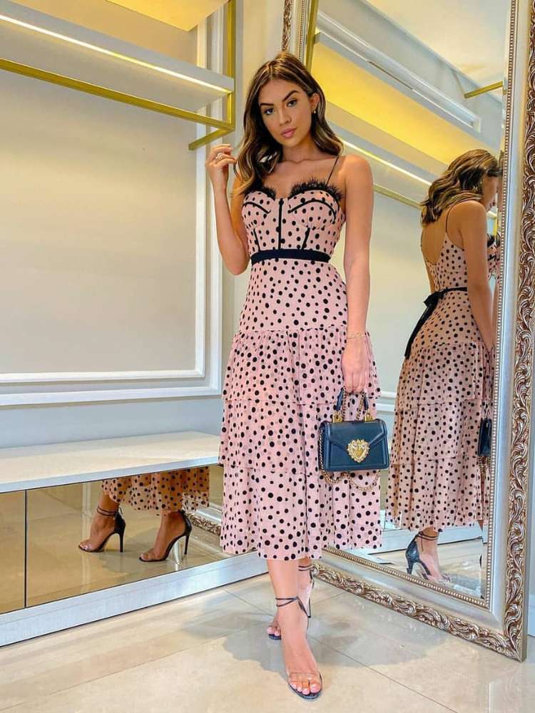 Mulher de pele morena usando vestido midi rosa com bolinhas pretas e salto