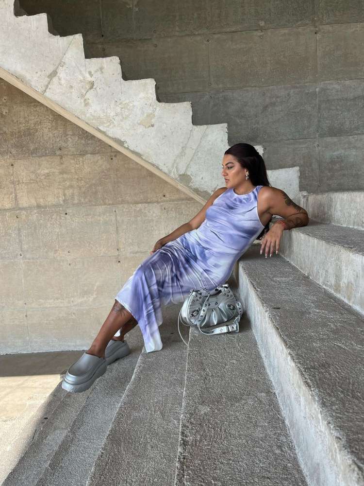 Mulher de pele morena sentada na escada usando vestido midi colorido e sandália prata
