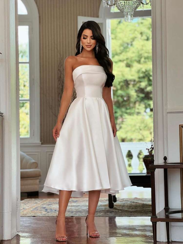 Mulher de pele clara e cabelo preto usando vestido midi branco tomara que caia e salto
