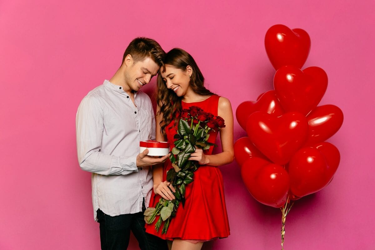 Casal com presentes, rosas e balões em formato de coração