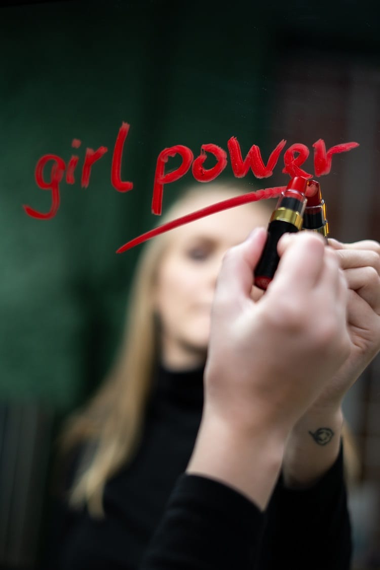 mulher loira escrevendo "girl power" no espelho com batom vermelho