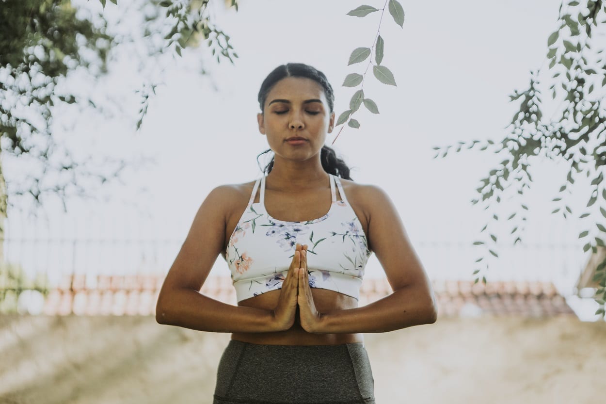 mulher meditando em pé, buscando o equilíbrio, um dos conceitos que define o que é ayurveda
