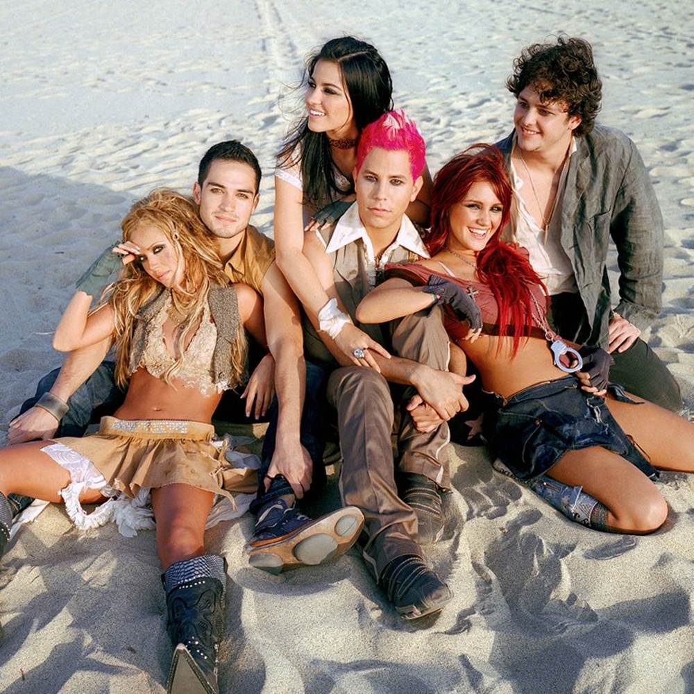 Homens e mulheres em foto na areia. Foto artística dos integrantes de RBD.