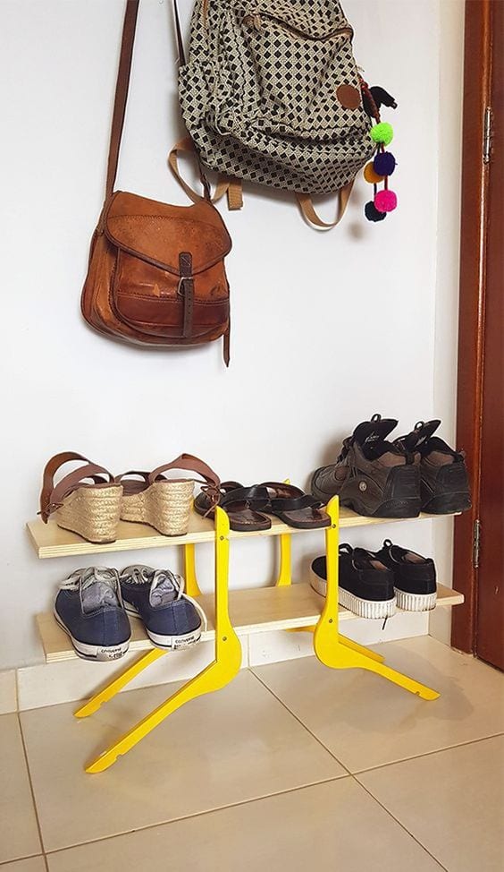 Duas prateleiras de madeira apoiadas por cabides. Nelas, estão colocados cinco pares de sapatos. Acima da sapateira, há duas bolsas penduradas. 