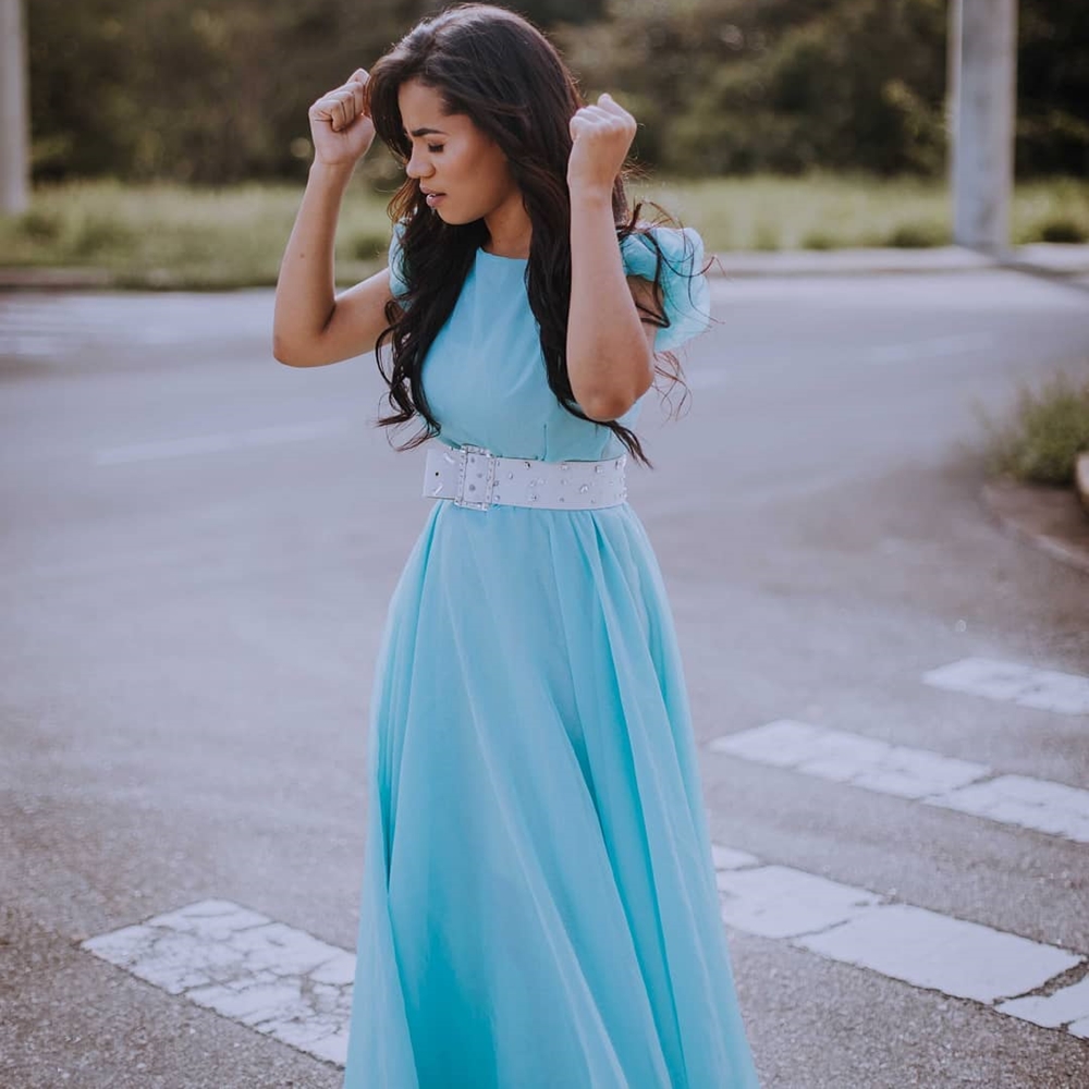 Stefhany Souza usa vestido azul e cinto branco. Cantora em foto, em momento do clipe.