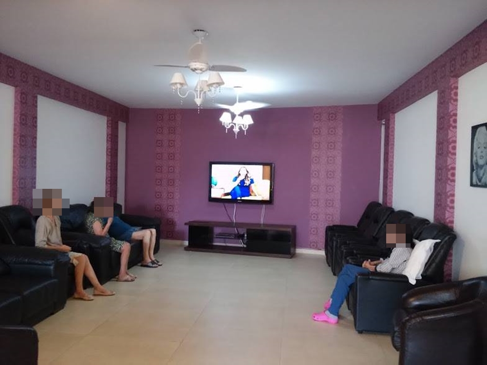 Sala de estar, paredes roxas, sofás pretos e televisão. Asilo Barros. Sala de estar com sofás e televisão