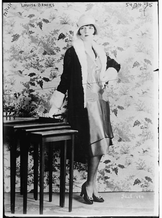 Foto da atriz Louise Brooks posando com um vestido curto e chapéu clochê, por volta de 1929. Look da Moda e Cidadania nos anos 20 e 30.