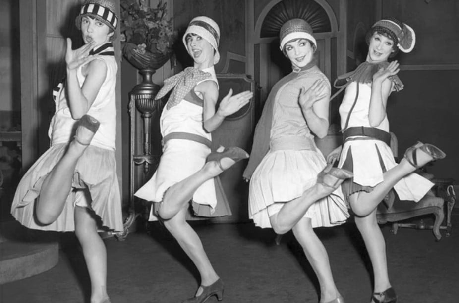 Mulheres dançando nos anos 30, com chapéu clochê e vestidos mais curtos. Look da Moda e Cidadania nos anos 20 e 30.