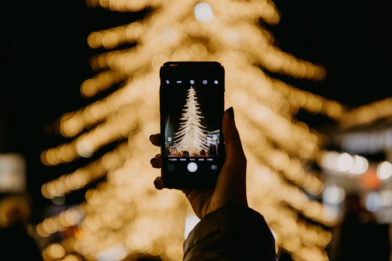 pessoa tirando foto de árvore com o celular para enviar mensagens de Natal