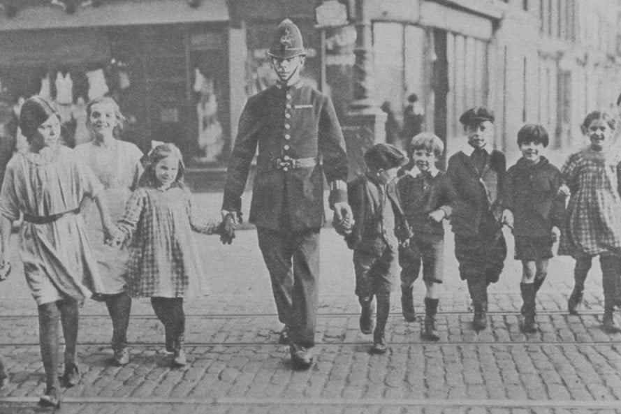 Grupo de crianças em Londres sendo guiadas por um policial, em 1920. 