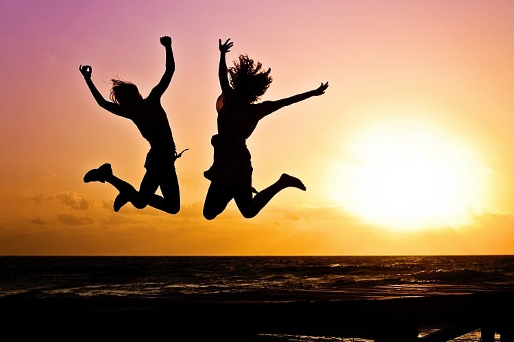 duas silhuetas de mulheres pulando com pôr do sol ao fundo