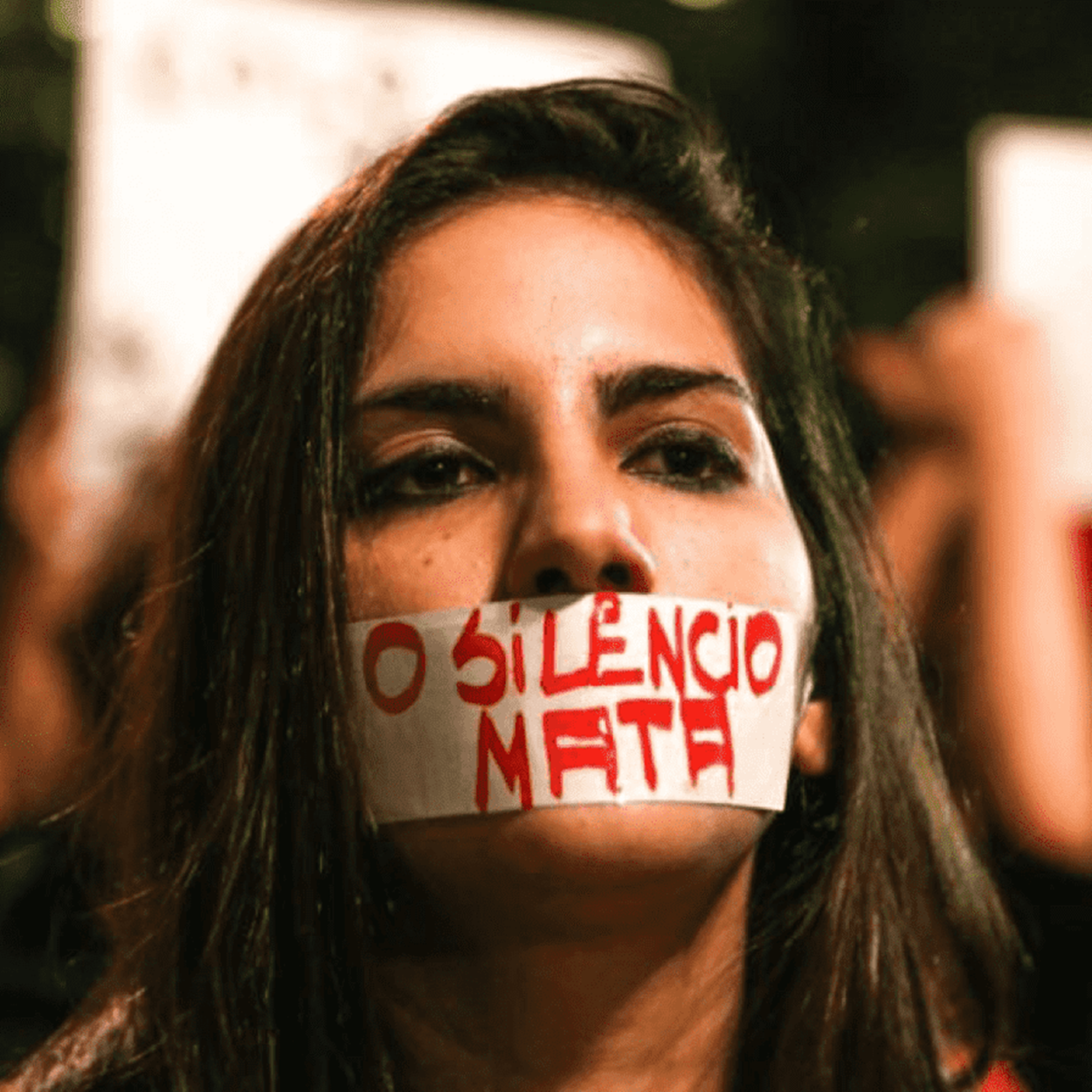 Mulher com fita na boca, escrito: "O silêncio mata"