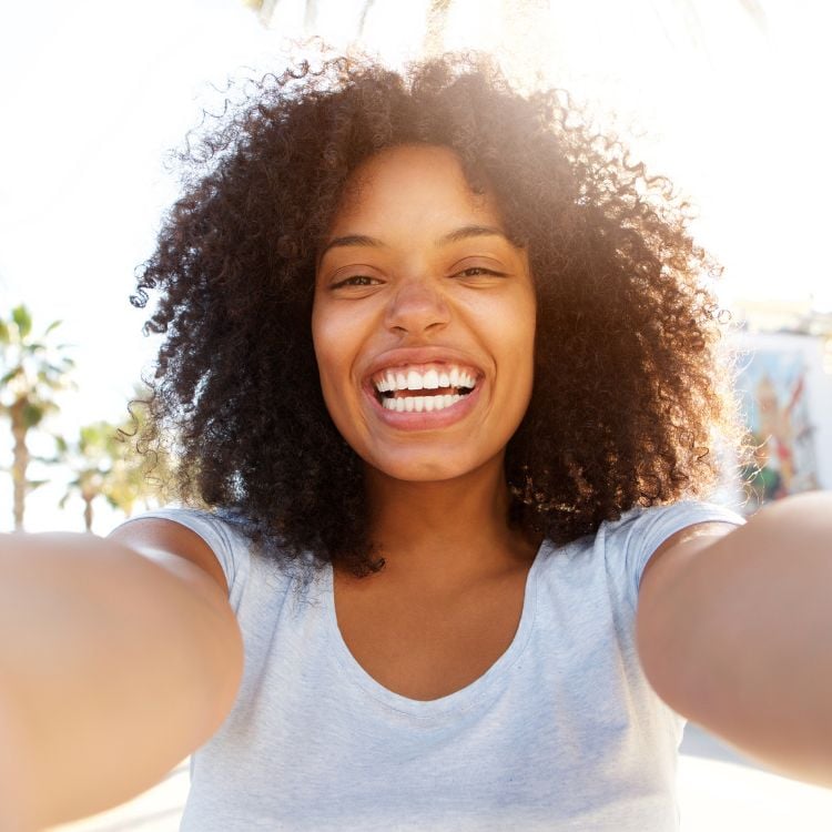 Selfie de mulher de pele negra sorrindo e usando blusa branca