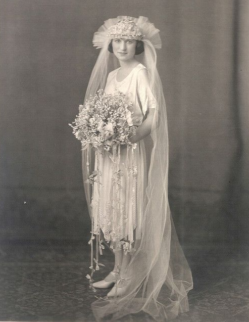 Noiva com vestido, chapéu, véu e buquê típicos de 1920.