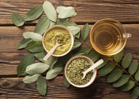 xícara de chá de moringa ao lado da folha fresca, seca e em pó